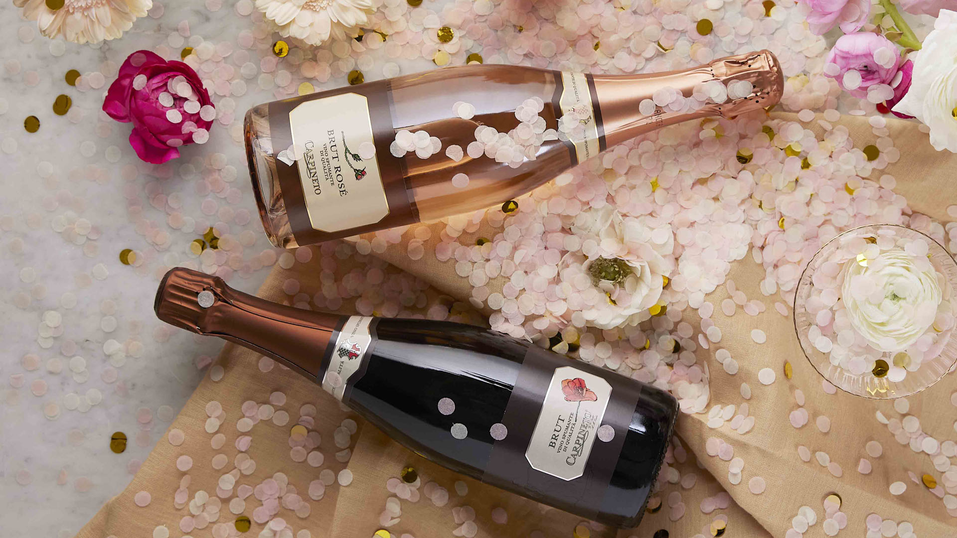 Bottiglie di Spumante Brut Rosé Carpineto tra petali e coriandoli rosa, ideale per brindisi eleganti e forniture HoReCa di alta gamma.